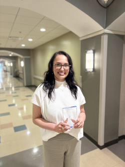 Woman stands in hallway holding plaque, smiling