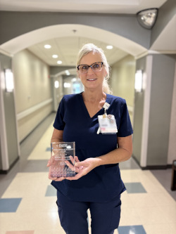 Woman stands in hallway holding plaque, smiling